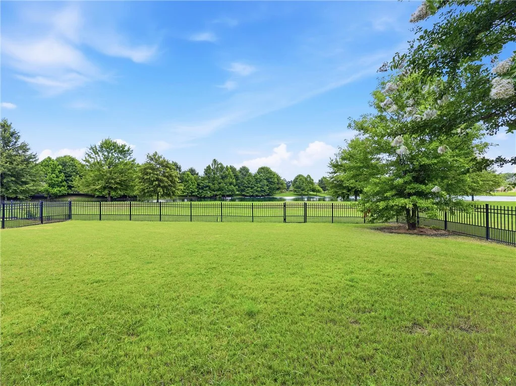 A verdant backyard with lake views, enclosed by sleek black fencing.