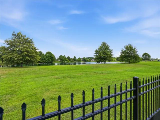A tranquil view of verdant fields bordered by a shimmering pond under a boundless sky.