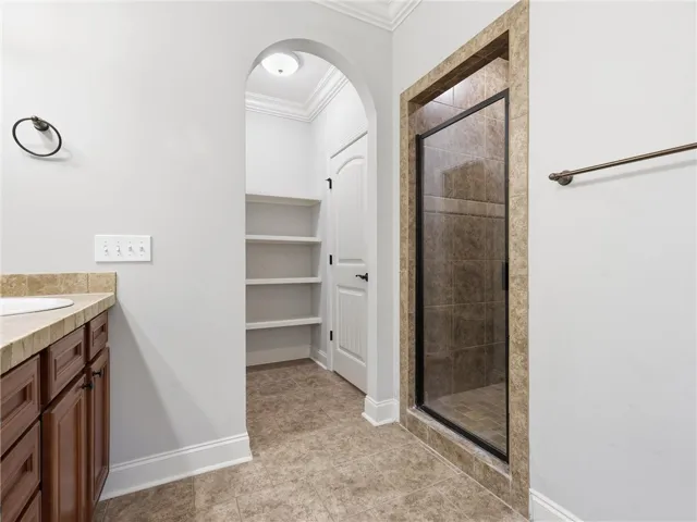 Functional bathroom features a glass-enclosed shower, ample storage shelving, and vanity.