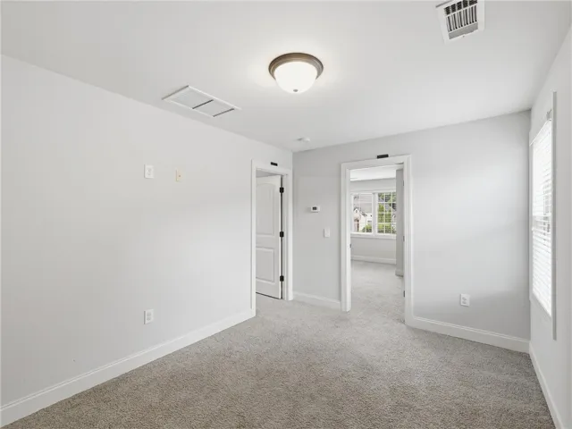 A well-lit interior space featuring neutral carpeting, a window providing natural illumination, and crisp white trim.
