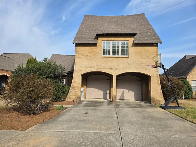 A classic brick facade welcomes with dual garage entrances and a dormer window above.