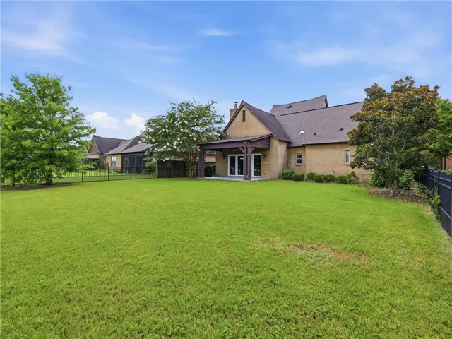 A spacious, well-maintained lawn stretches behind a brick residence, featuring a covered patio and secure fencing.