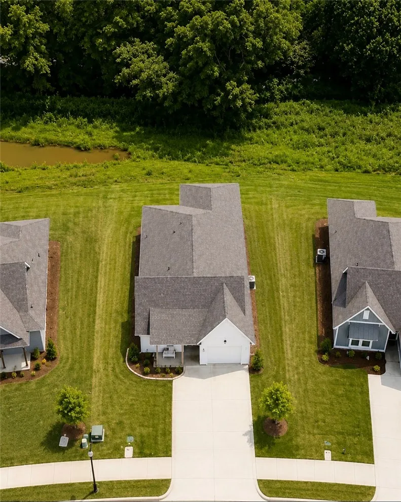 An aerial perspective reveals a modern home nestled in a well-kept neighborhood, boasting verdant lawns and tranquil views of surrounding nature.