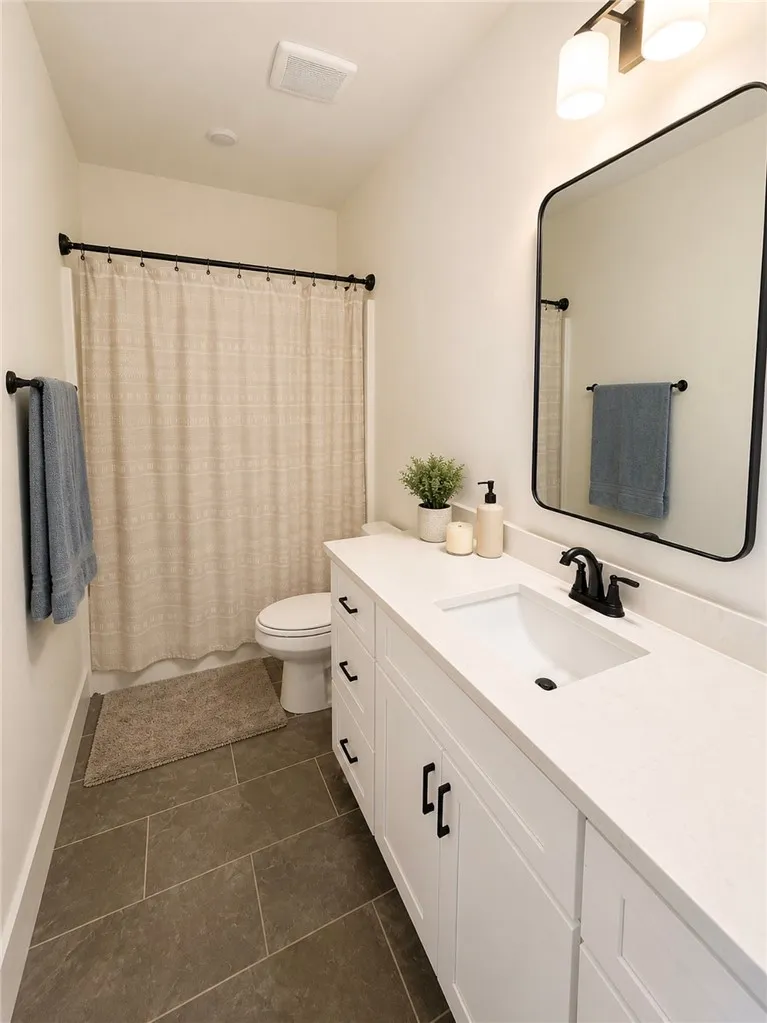 A pristine bathroom features clean white cabinetry and dark tile flooring, offering practical elegance.