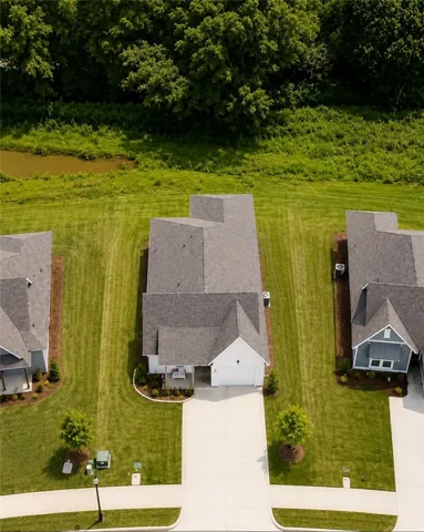An aerial perspective reveals a modern home nestled in a well-kept neighborhood, boasting verdant lawns and tranquil views of surrounding nature.