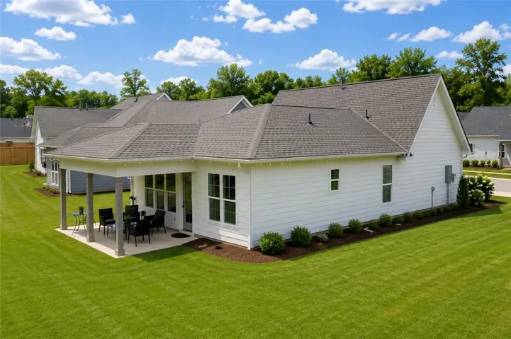 A sprawling green lawn borders a pristine, newly constructed residence with a charming covered patio.