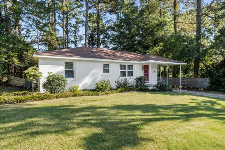 A charming single-level residence nestled among mature trees, featuring a welcoming front porch and well-maintained lawn.