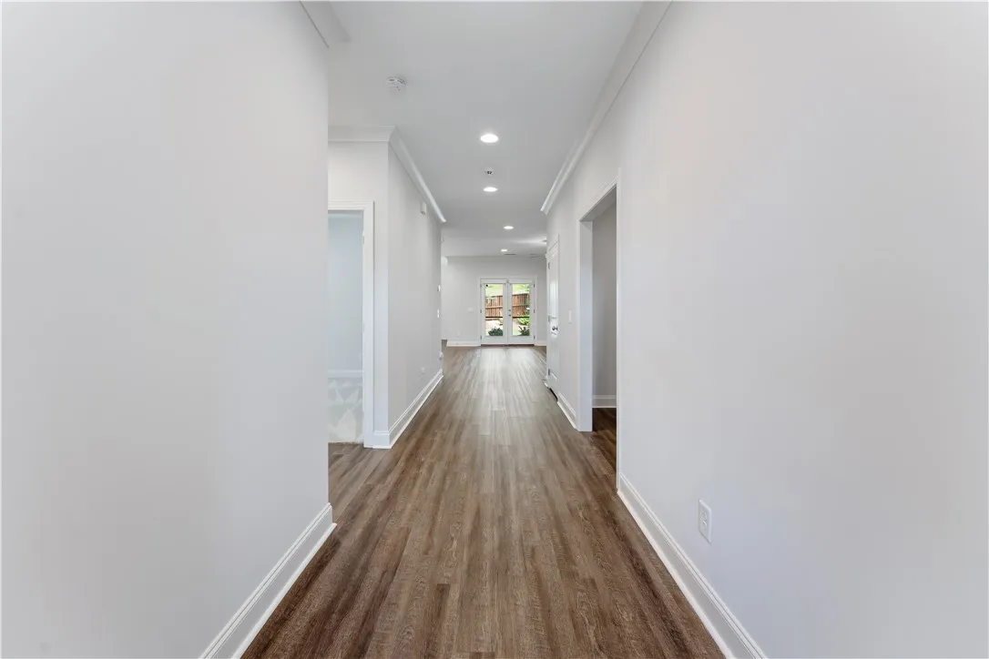 A long, inviting hallway with recessed lighting leads to French doors opening to the outdoors.