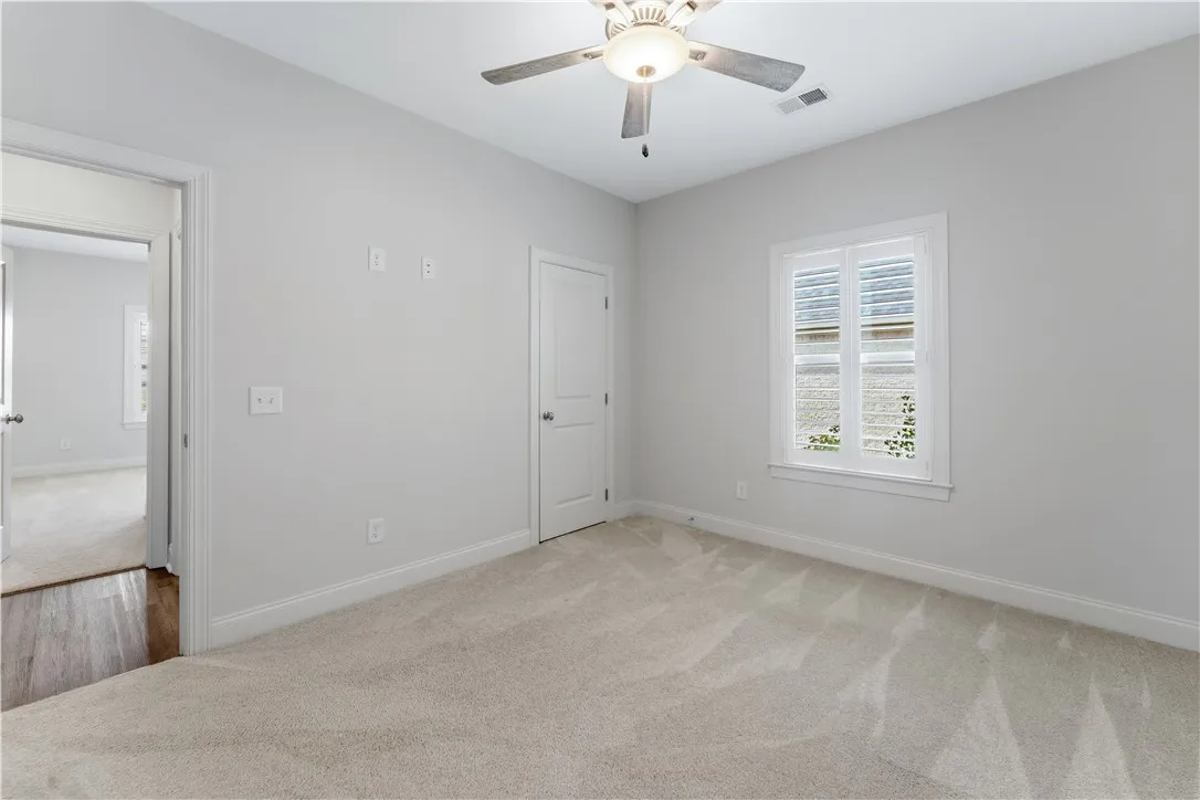 A well-lit room offering plush carpeting and a bright window with classic plantation shutters.