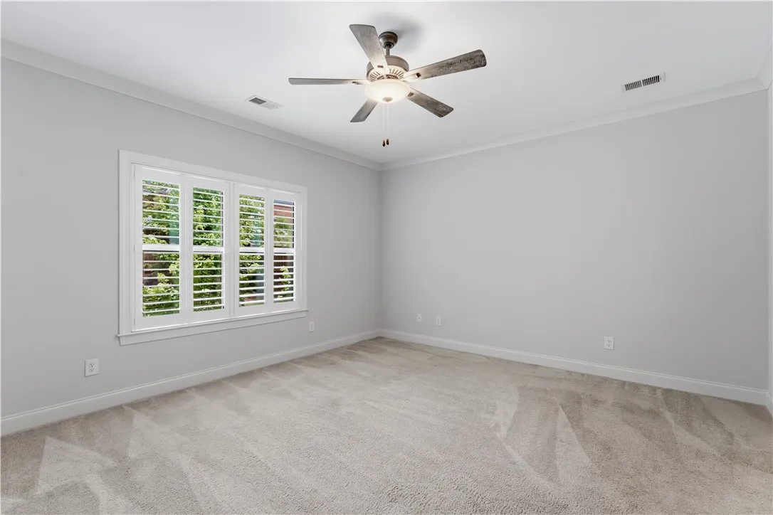 An airy bedroom with a ceiling fan and a window featuring plantation shutters, offering ample natural light.