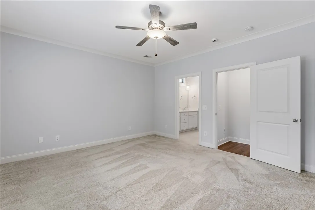 A spacious bedroom featuring comfortable carpeting and a modern ceiling fan, offering direct access to an ensuite bathroom.