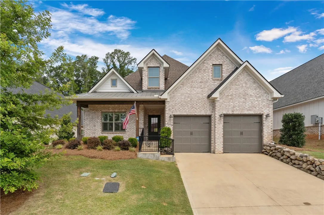A charming brick exterior with a welcoming front porch and attached garages, set amidst neat landscaping.