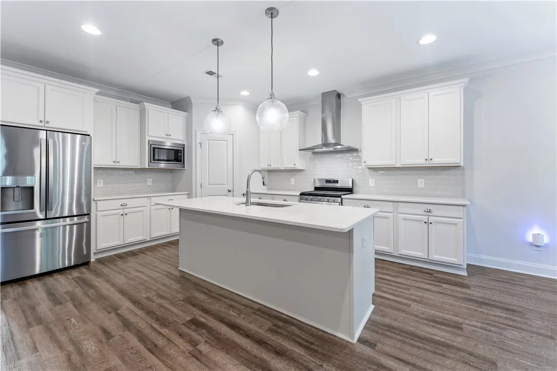 A well-lit kitchen with sleek stainless steel appliances, a generous island, and rich hardwood flooring.