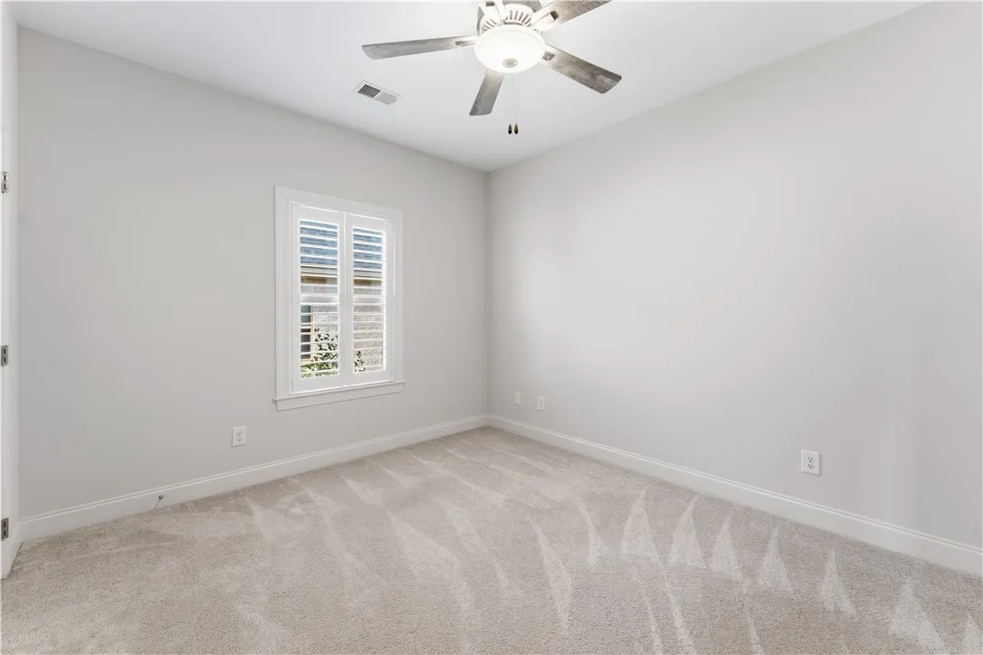 A well-lit bedroom with fresh carpeting and a practical ceiling fan.
