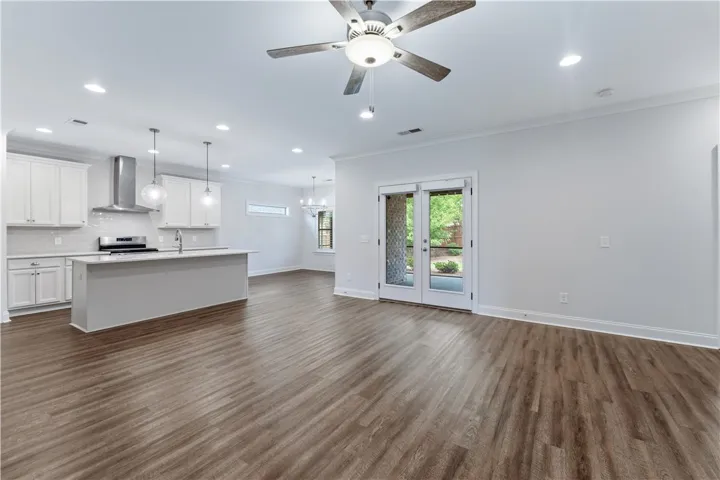 An open-concept living space features a modern kitchen island, wood-look flooring, and a glass-paneled double door leading to the exterior.