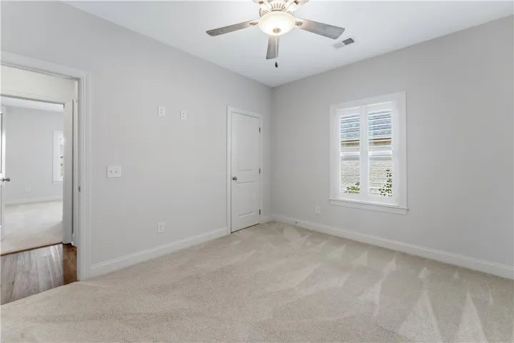 A well-lit room offering plush carpeting and a bright window with classic plantation shutters.
