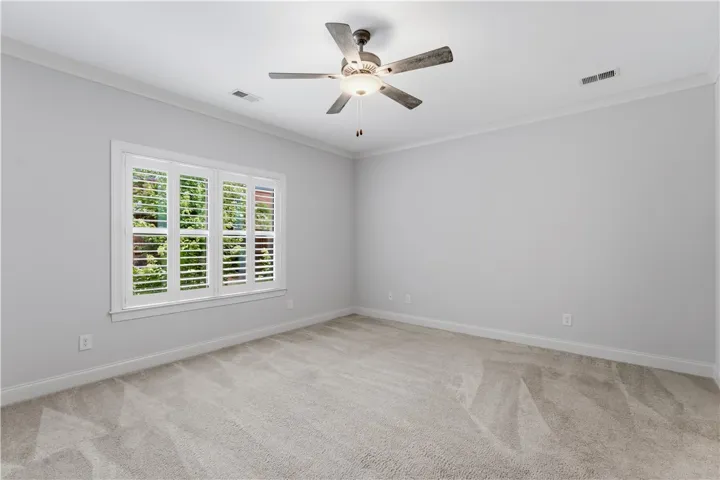 An airy bedroom with a ceiling fan and a window featuring plantation shutters, offering ample natural light.