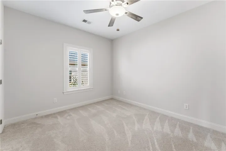 A well-lit bedroom with fresh carpeting and a practical ceiling fan.