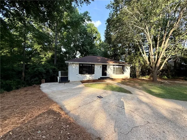 A well-maintained facade awaits, featuring a concrete driveway and mature shade trees.