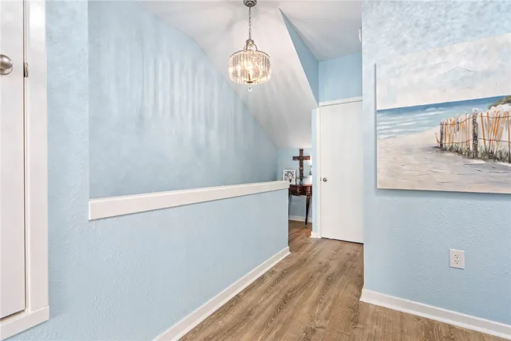 Laminate flooring extends through this gracefully lit interior hallway, featuring a sparkling chandelier.
