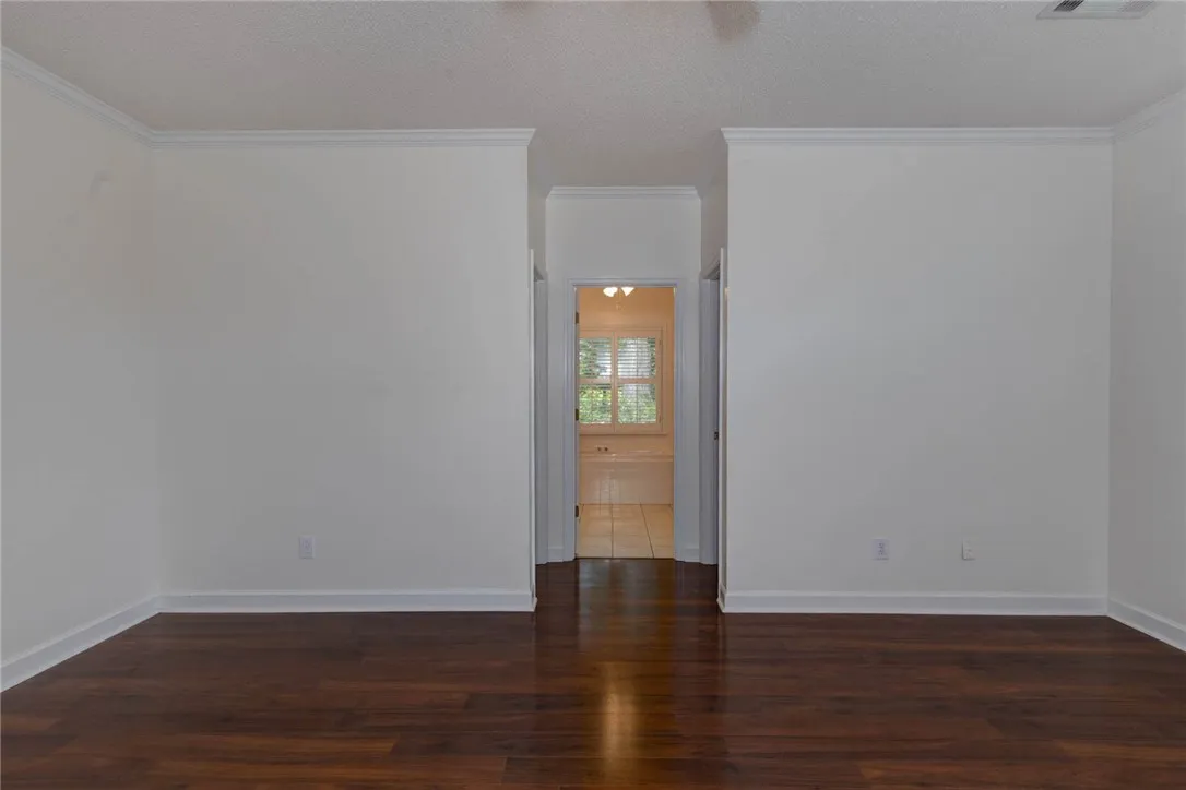 Rich hardwood flooring creates a welcoming ambiance, leading towards a sunlit view through a distant window.
