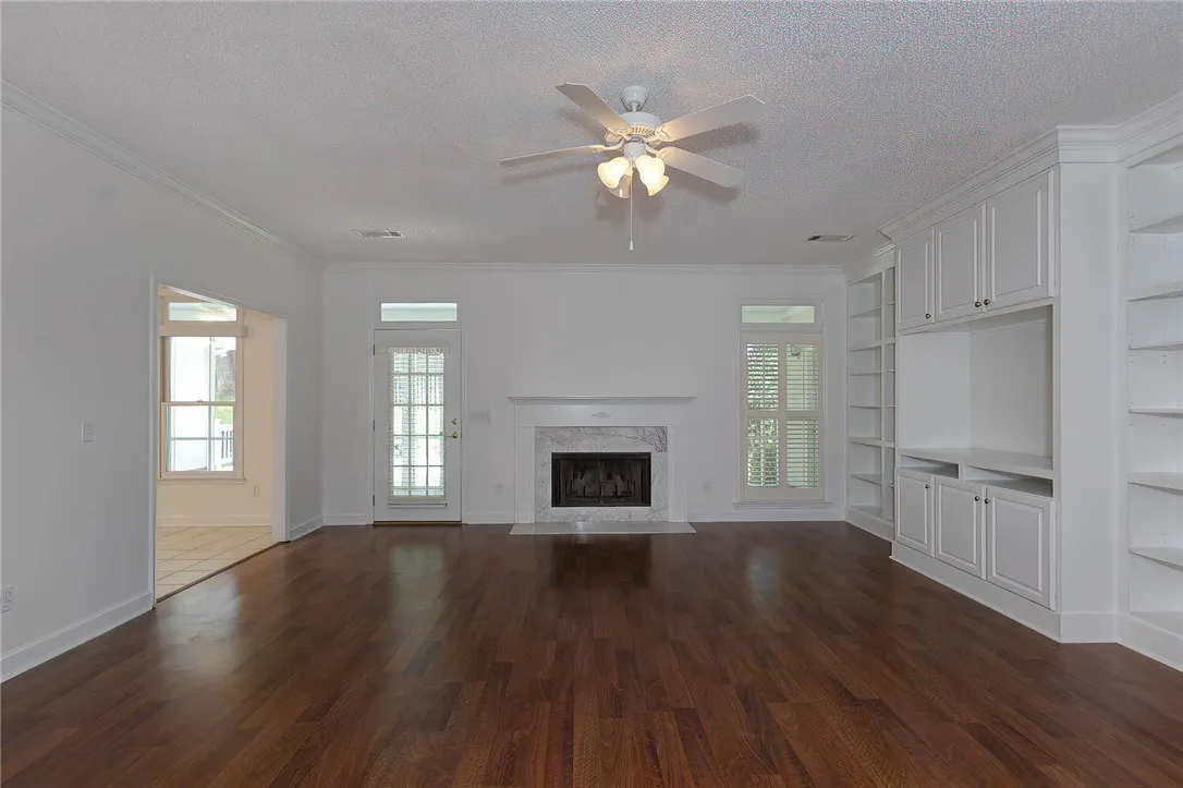 Rich hardwood flooring complements a fireplace with a marble surround and custom built-in shelving.