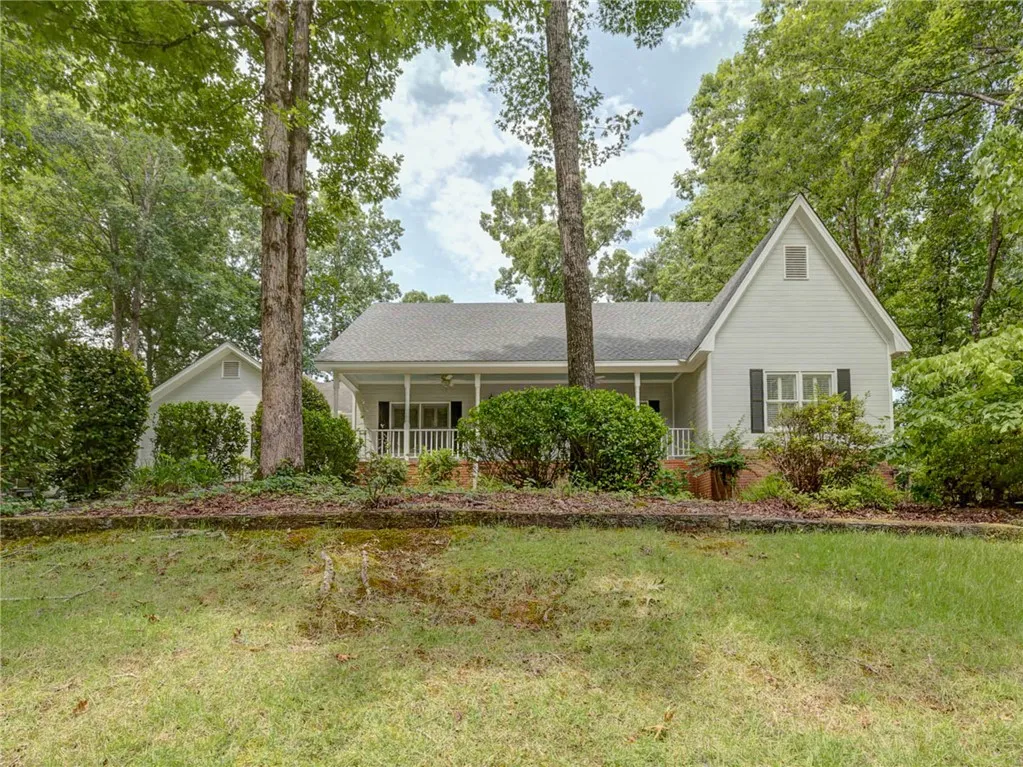 A charming single-story residence nestled among mature trees, featuring a welcoming covered front porch.