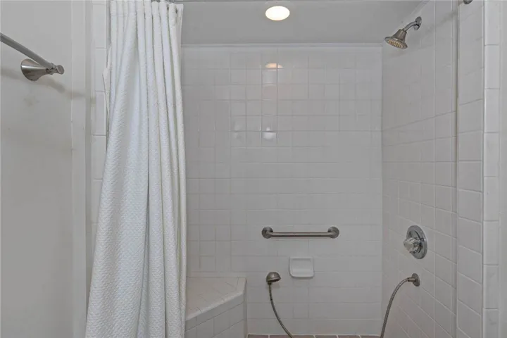 A well-lit shower features accessible seating and a convenient handheld sprayer.
