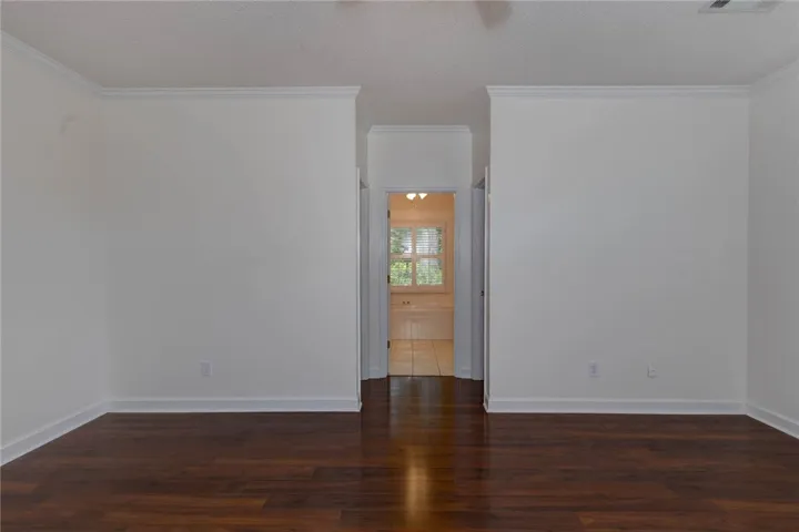 Rich hardwood flooring creates a welcoming ambiance, leading towards a sunlit view through a distant window.