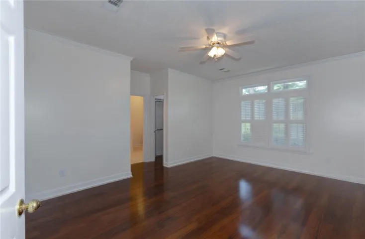 Rich hardwood flooring complements a spacious bedroom featuring a window with natural light.