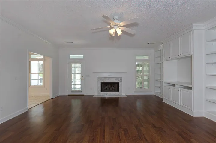 Rich hardwood flooring complements a fireplace with a marble surround and custom built-in shelving.