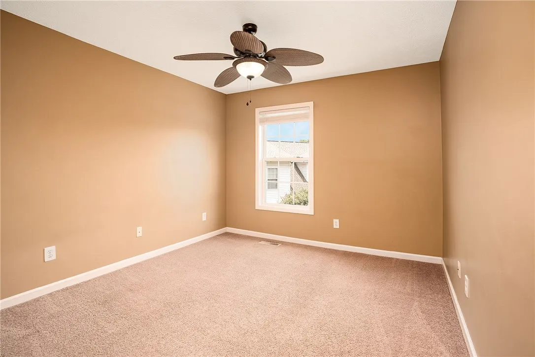 A well-lit bedroom features plush carpeting and a modern ceiling fan, offering comfortable living.