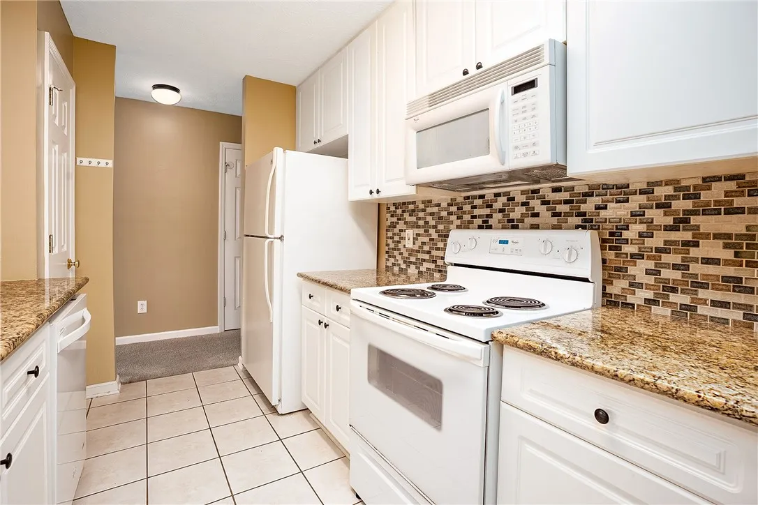 A compact kitchen offering granite countertops and a charming tile backsplash.