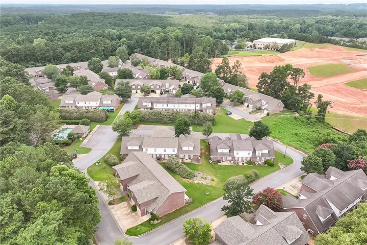 An aerial perspective reveals a vibrant community with townhomes nestled among lush trees, featuring a sparkling community pool.