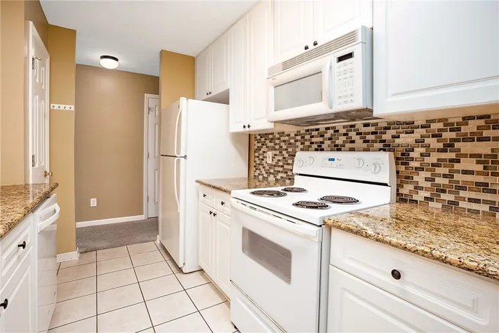 A compact kitchen offering granite countertops and a charming tile backsplash.