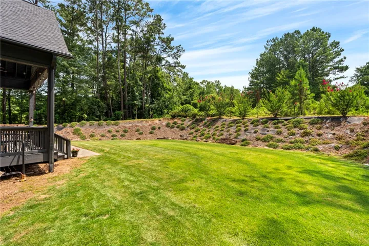 A spacious backyard unfolds, framed by a welcoming porch and a tree-lined hillside.