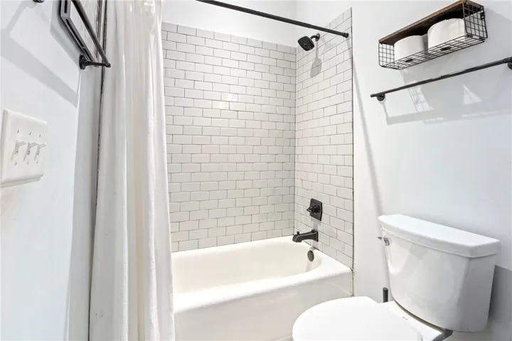 A fresh, clean bathroom offers a pristine subway tile tub and a functional toilet.