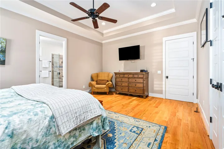 Hardwood floors and tray ceilings elevate this well-lit primary bedroom, complete with an attached bathroom.