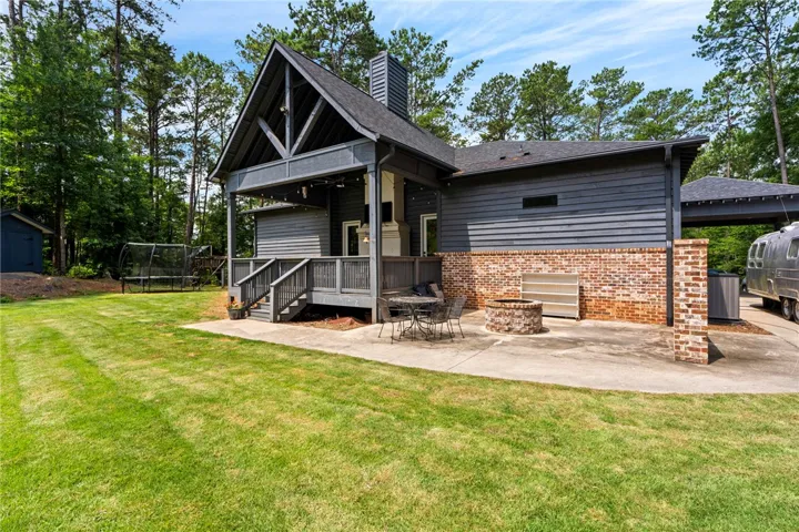 A welcoming rear exterior combines a covered deck, patio, and fire pit, all set against a backdrop of mature trees.