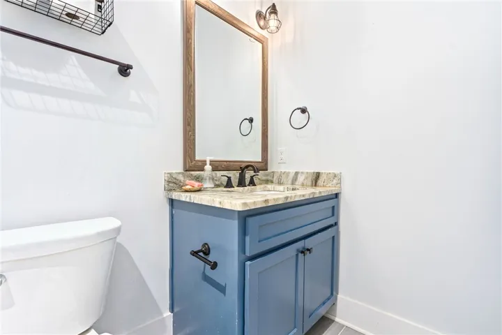 A refined bathroom featuring a contemporary vanity with a natural stone countertop and a warm wood-framed mirror.