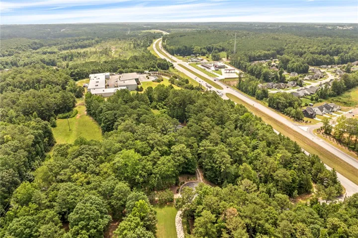 An aerial perspective reveals the property's serene, tree-lined landscape adjacent to a bustling highway and residential community.