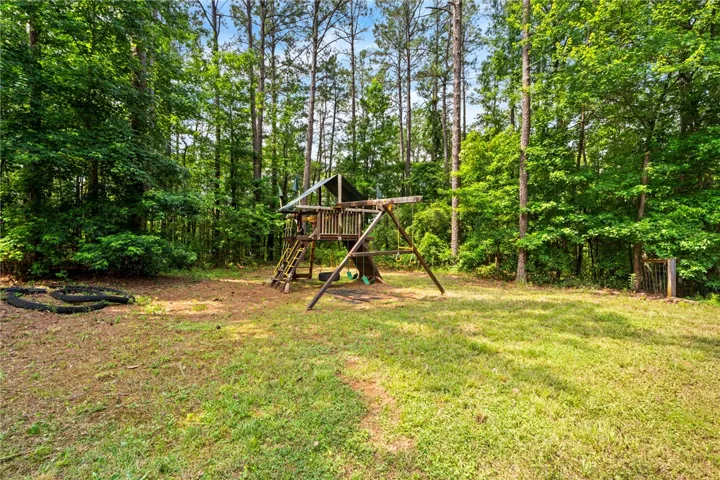 A spacious backyard with mature trees surrounds a playful wooden playset.
