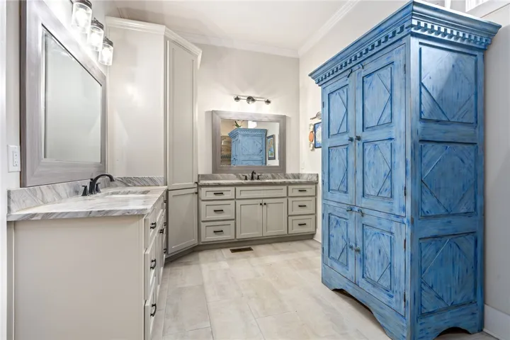 Marble-look counters and gray tile flooring complement the dual vanities and rustic blue storage cabinet.
