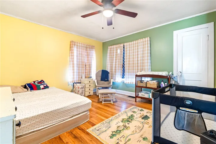 Hardwood floors and a ceiling fan with light fixture enhance this well-appointed bedroom.