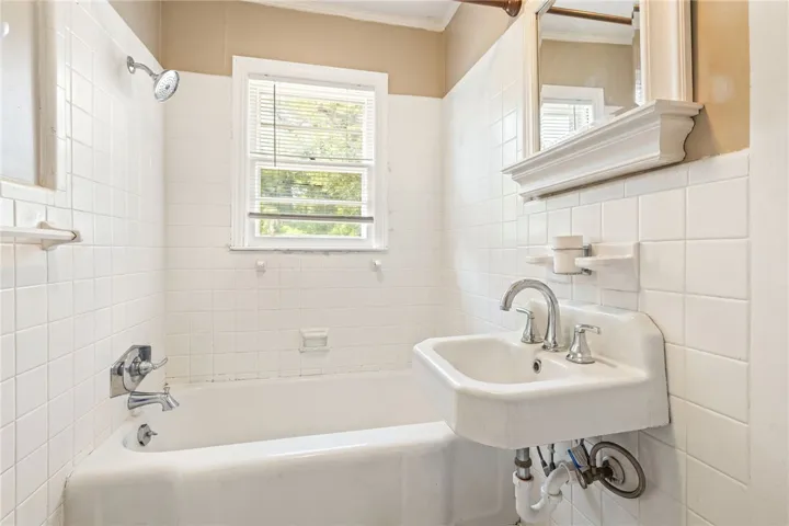 A compact bathroom offers essential fixtures, a window, and fully tiled walls for easy maintenance.