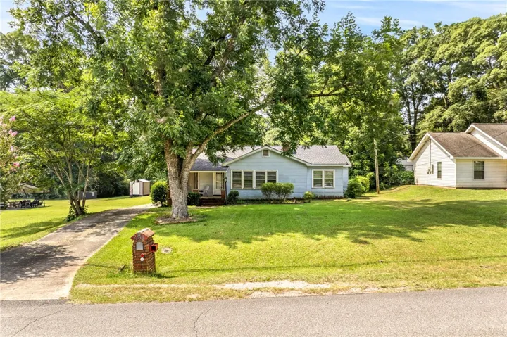 A charming light-blue home nestled amidst verdant landscaping and mature shade trees.