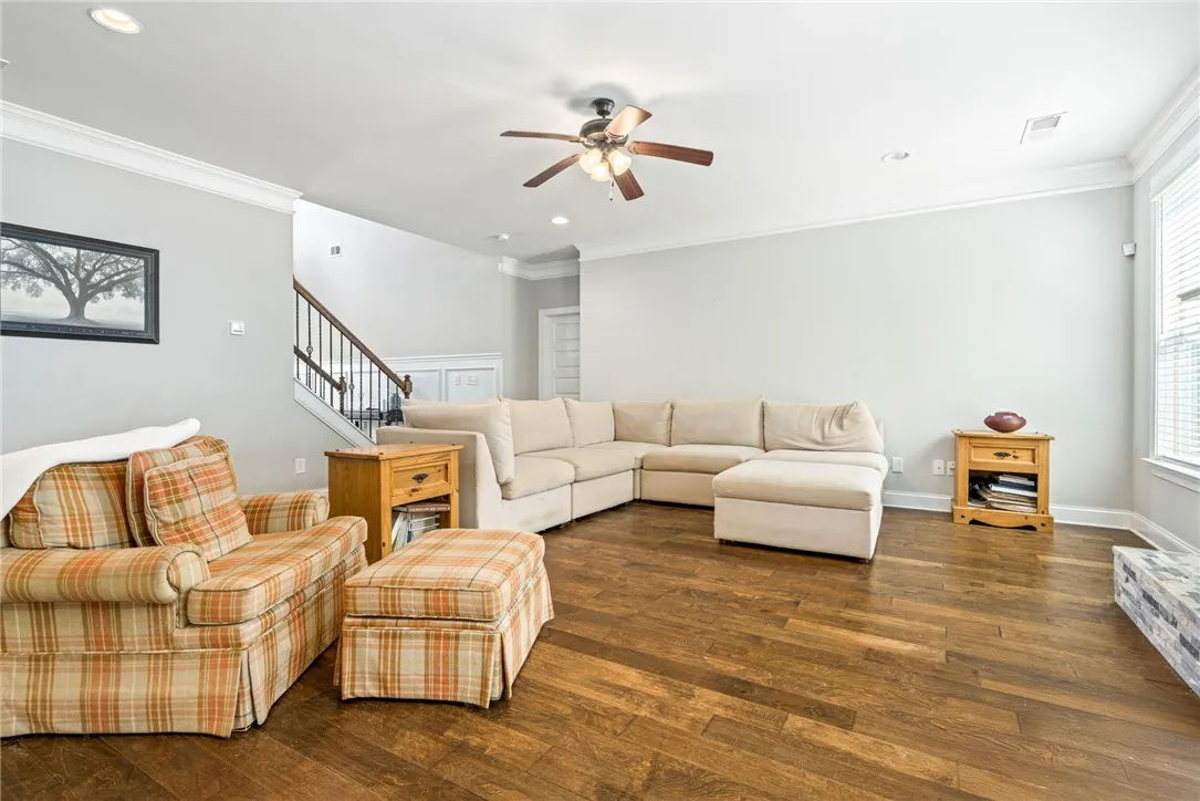 Rich hardwood floors complement a spacious living area with an elegant staircase and subtle ceiling fan.