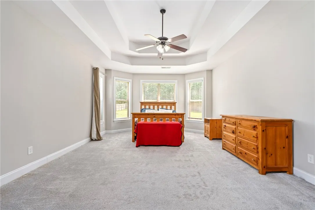 A spacious primary bedroom features a striking tray ceiling, plush carpeting, and abundant natural light.