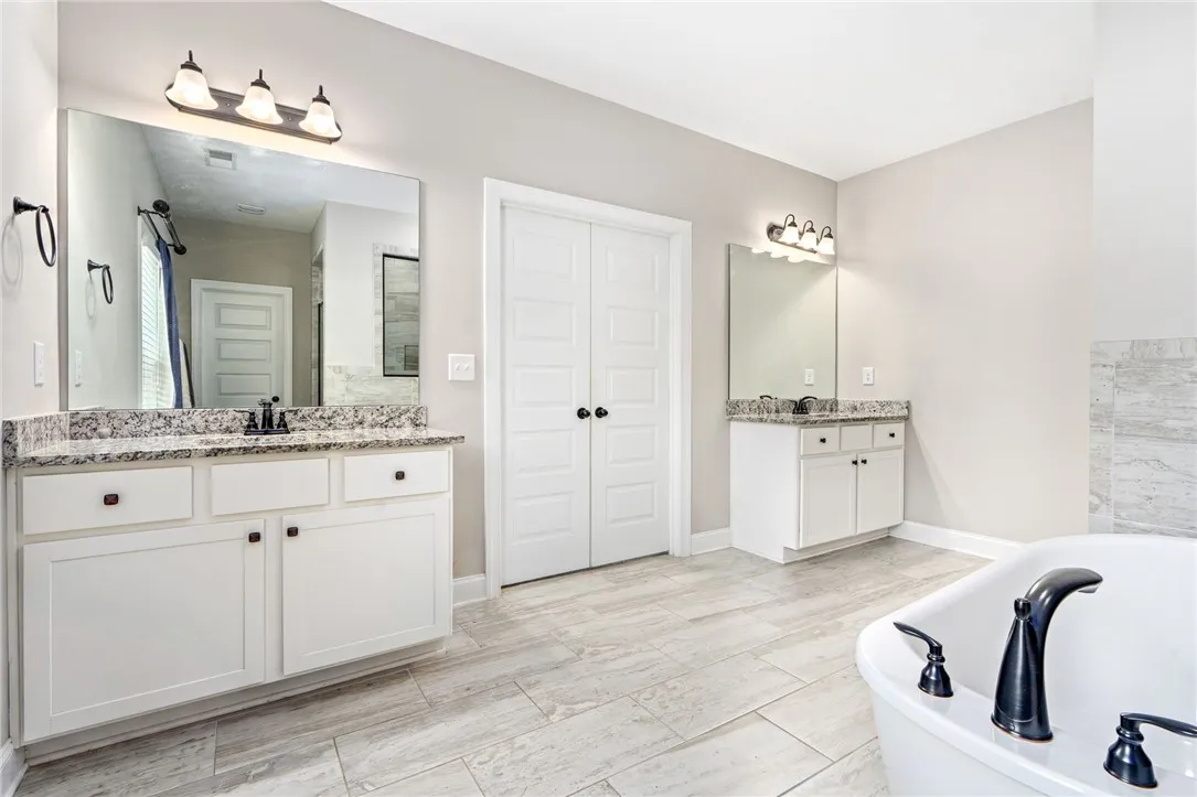 Luxurious primary bathroom featuring a freestanding tub, separate vanities, and durable tile flooring.