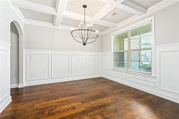 Hardwood flooring flows through this bright dining area, featuring classic wainscoting and a distinctive coffered ceiling.